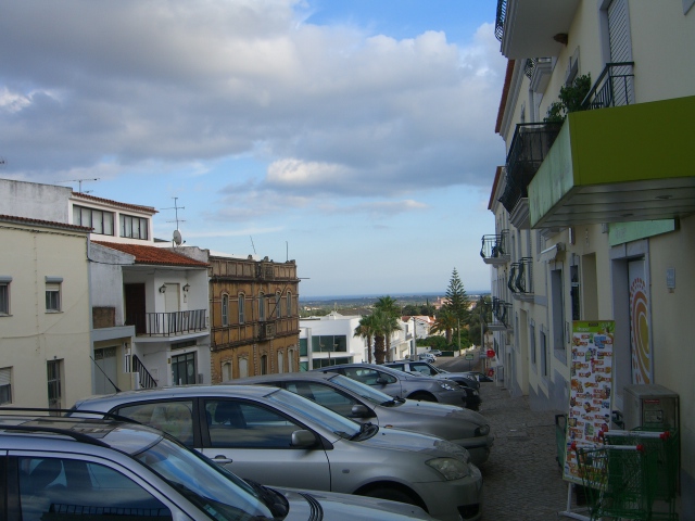 Grey cars, buildings old and new, sea in the distance.